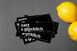 Schwarze Sticker mit Aufschrift: satt und glücklich. Und zwei Zitronen.