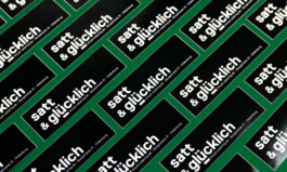 Schwarze Sticker mit Aufschrift: satt und glücklich. Auf dunkelgrünem Hintergrund.