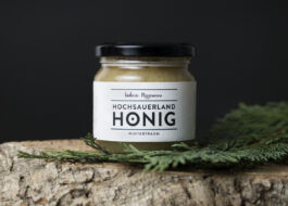 Im Zentrum steht der Wintertraum-Honig auf einem Holzstück und einem Tannenzweig 